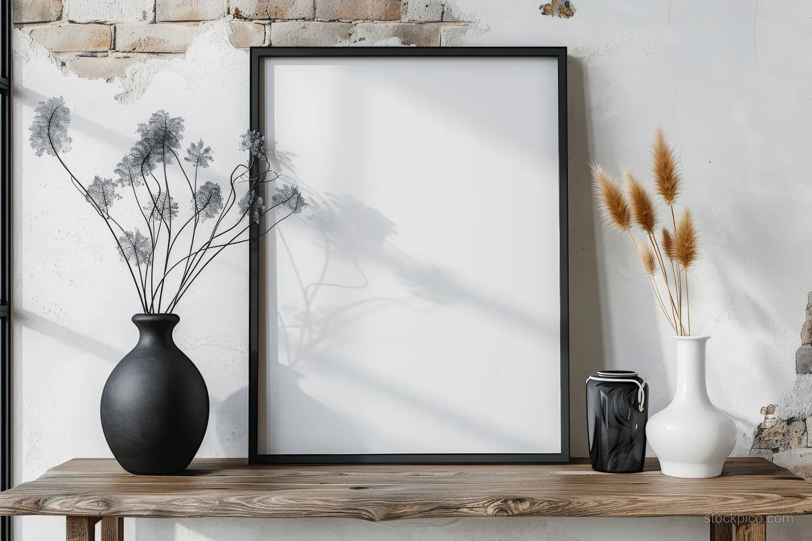 Blank white poster in a black frame on a wooden console with a black vase and thistles in soft light.