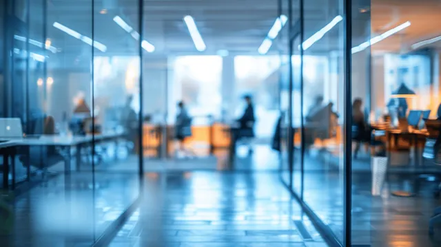 Blurred office hallway with coworkers working at desks and overhead light streaks on the floor.