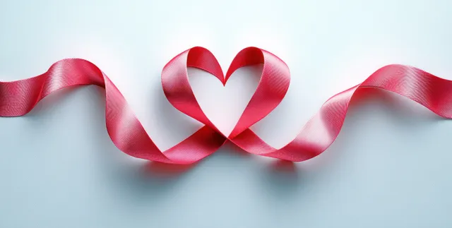 Red satin ribbon heart shape with flowing loops on clean light background