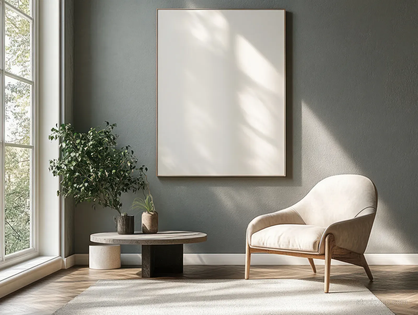 Sunlit minimalist gray living room showing an armchair, low coffee table, framed wall art, and potted plant by a window.