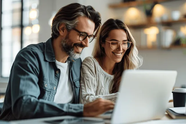Smiling man and woman managers collaborate on laptops in a minimalist modern office, both looking at their screens.