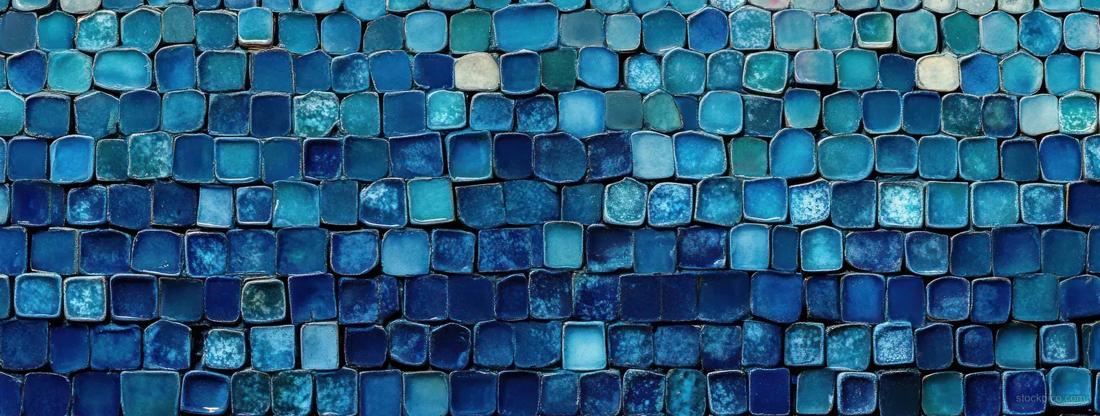 Close-up of a blue mosaic wall with square ceramic tiles, varied shades, and subtle glossy reflections.