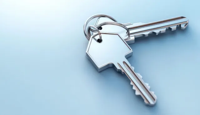 Silver house keys on a blue background with a metal keyring and sharp reflections.