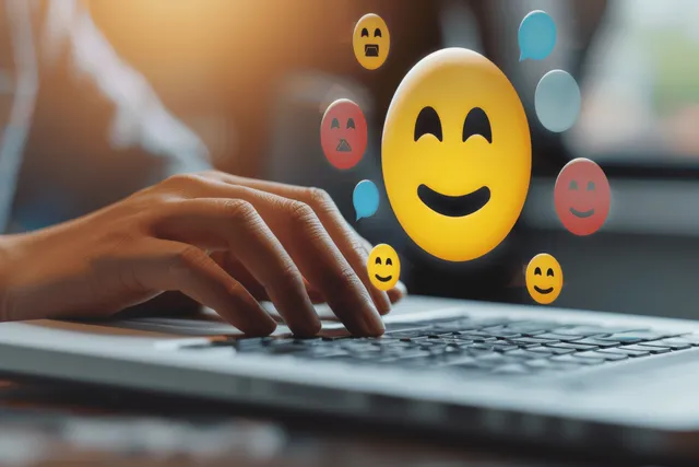 A man types on a laptop as emoji rating icons float over the screen during a satisfaction survey.