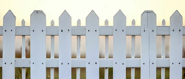 White wooden picket fence with evenly spaced vertical slats in daylight and a blurred background.