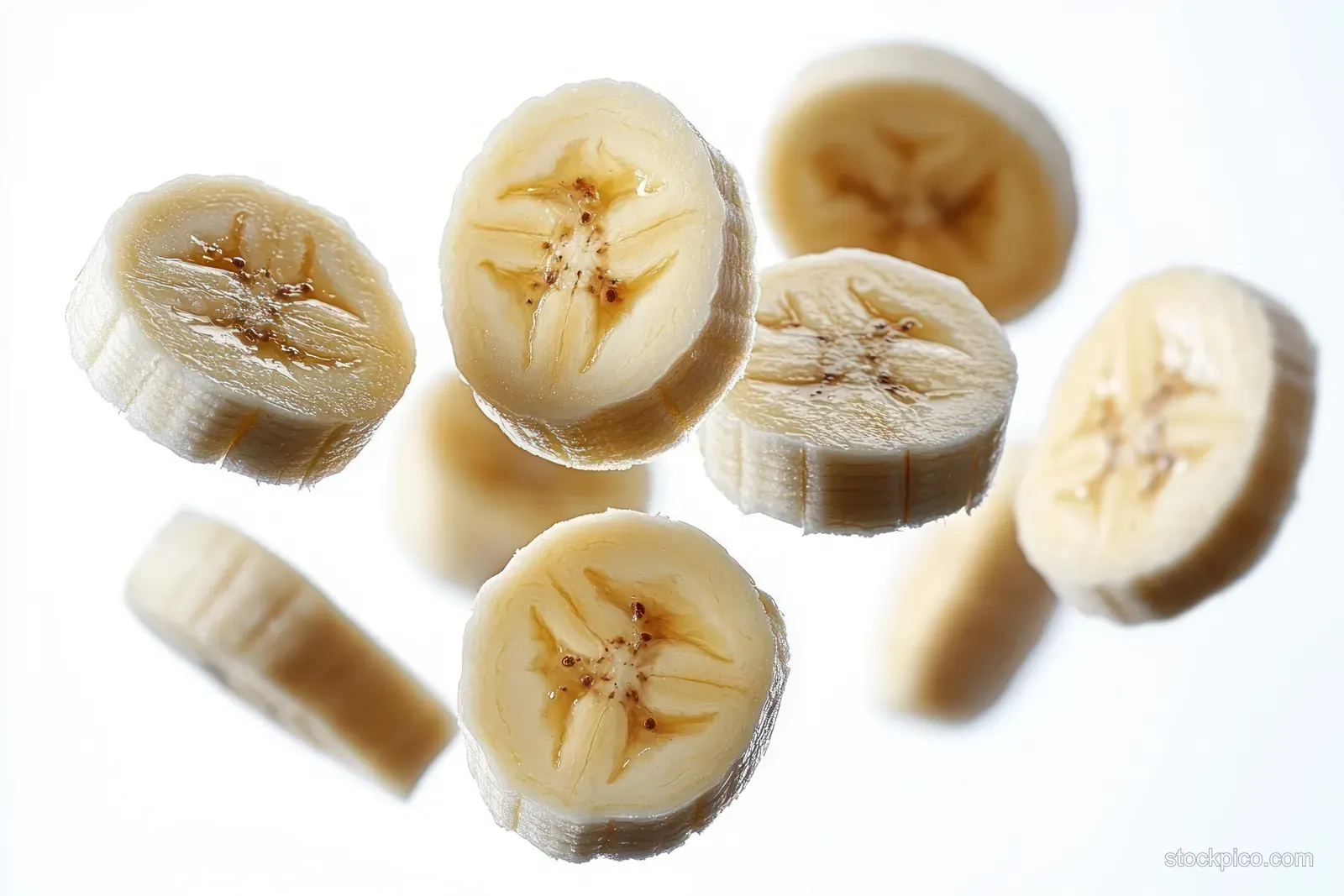 Banana slices falling on a white background, showing creamy interiors and natural seed patterns.