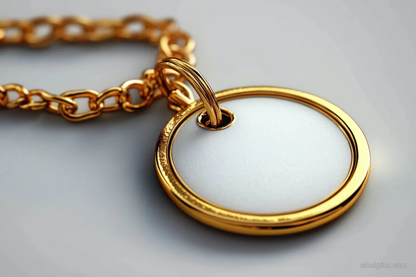 Shiny gold chain necklace with a round blank pendant on a soft grey background.