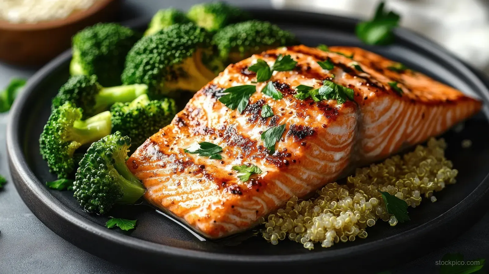 Grilled salmon fillet with parsley, steamed broccoli, and quinoa on a dark plate.
