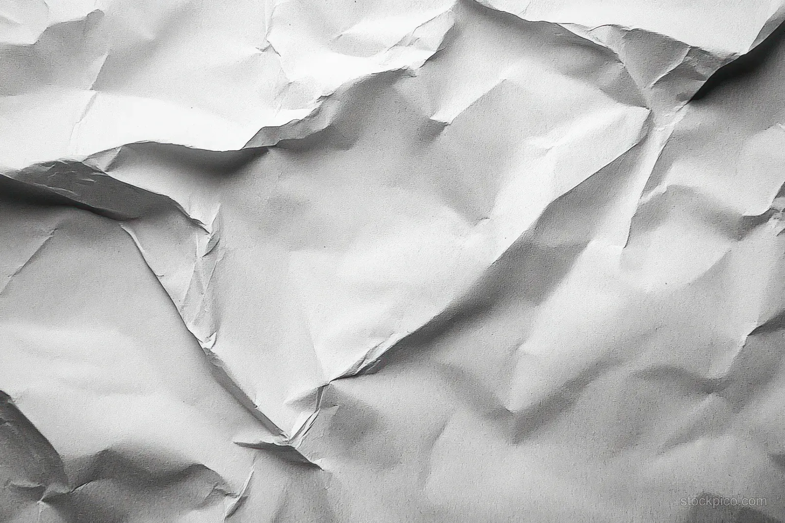Close-up of wrinkled white paper with irregular creases and shadows forming textured patterns.