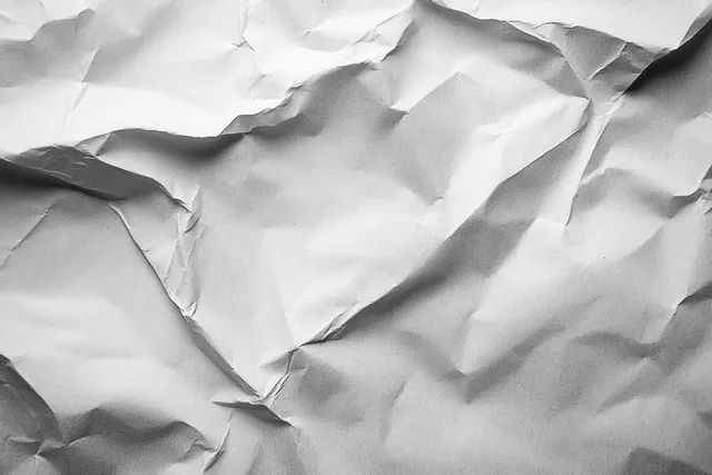Close-up wrinkled white paper surface with irregular folds and deep shadows