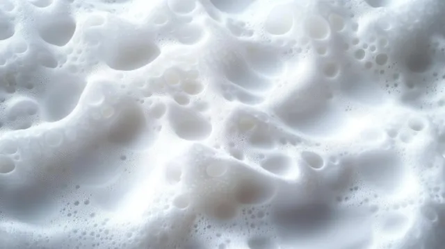 Close-up foam bubbles form a dense lather pattern across a wet white surface