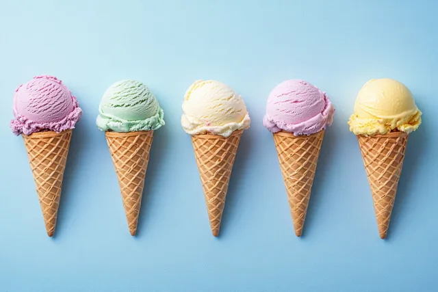 Five waffle ice cream cones with pastel scoops arranged in a row on a light blue background.