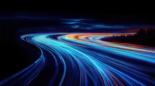 Curved highway at night with blue and orange long-exposure light trails streaking around a bend
