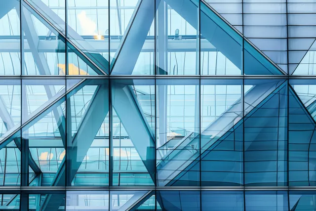 Triangular blue-gray glass facade with steel beams and grid reflections inside a modern building.