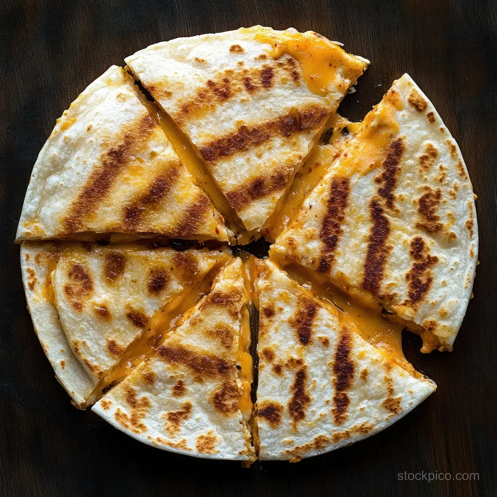 Sliced grilled quesadilla with melted cheddar cheese arranged in wedges on a dark wooden surface.