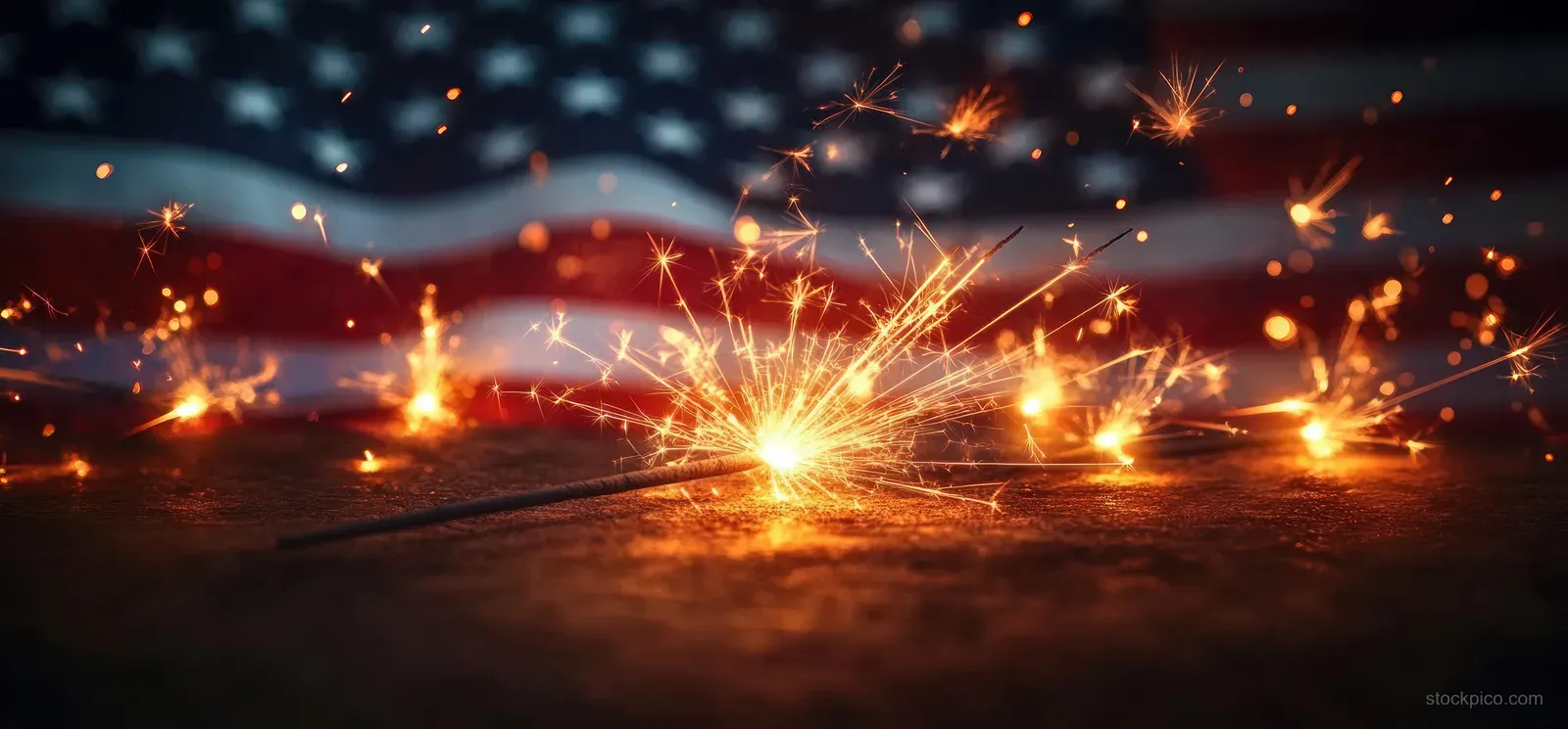 Sparklers flare with bright orange sparks across a dark Independence Day themed background.