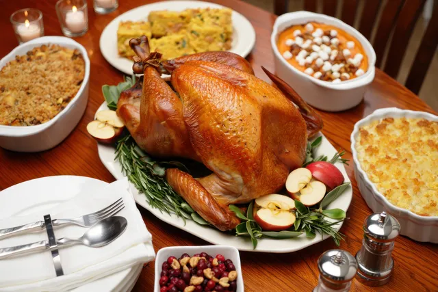 Roasted turkey centerpiece with rosemary on a wooden Thanksgiving table surrounded by side dishes and shakers.