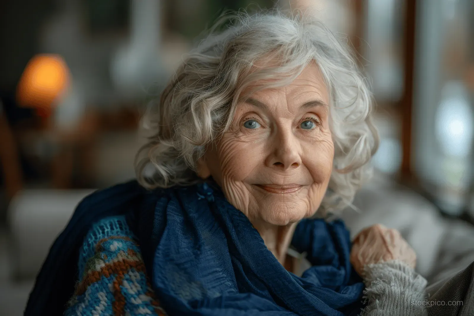 Elderly woman in navy yoga clothes smiles toward the camera in a sunlit living room.