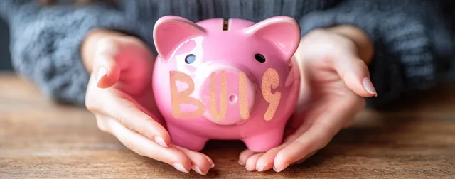 Hands holding a pink piggy bank on a wooden table, counting savings