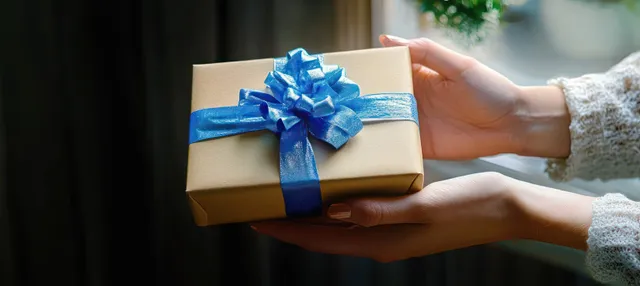 Hands exchanging a blue ribbon gift box with warm, soft background light