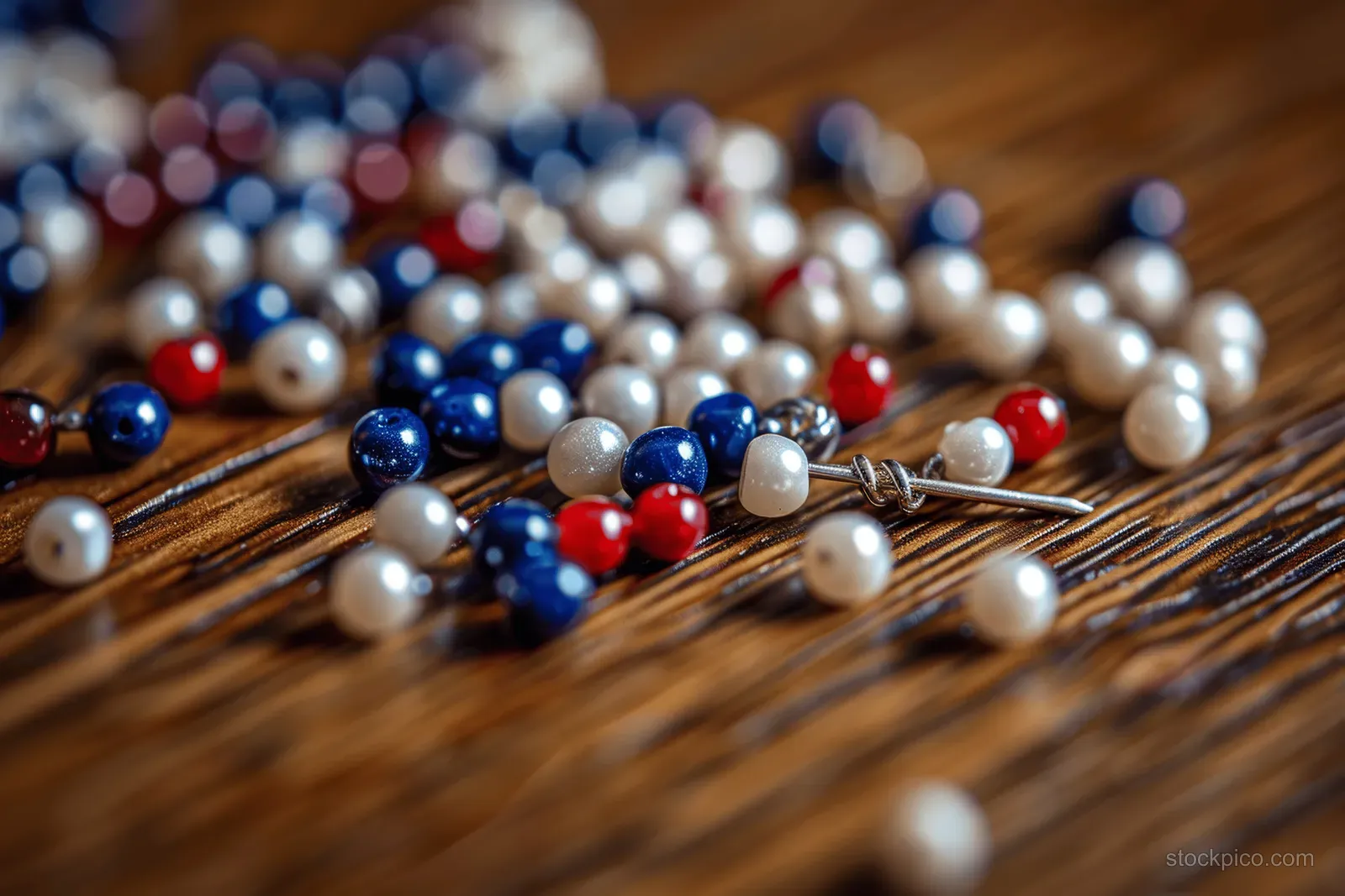 Colorful beads and a safety pin lie on a wooden table with blurred lights in the background.