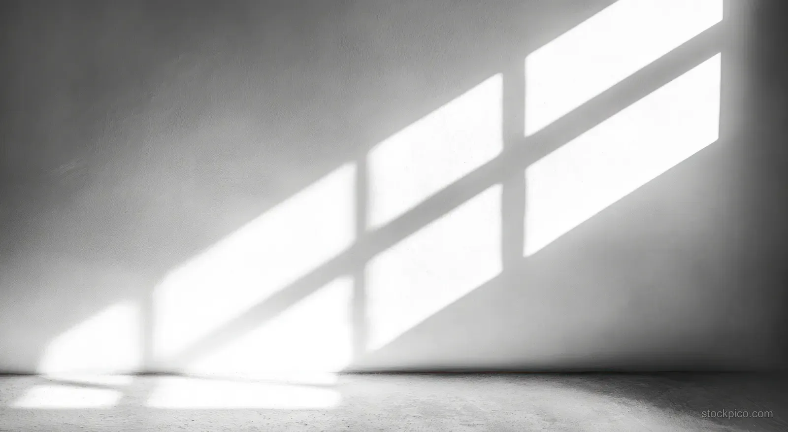 Sunlight beams through a window grid, casting geometric shadows on a textured wall and concrete floor in an empty room.