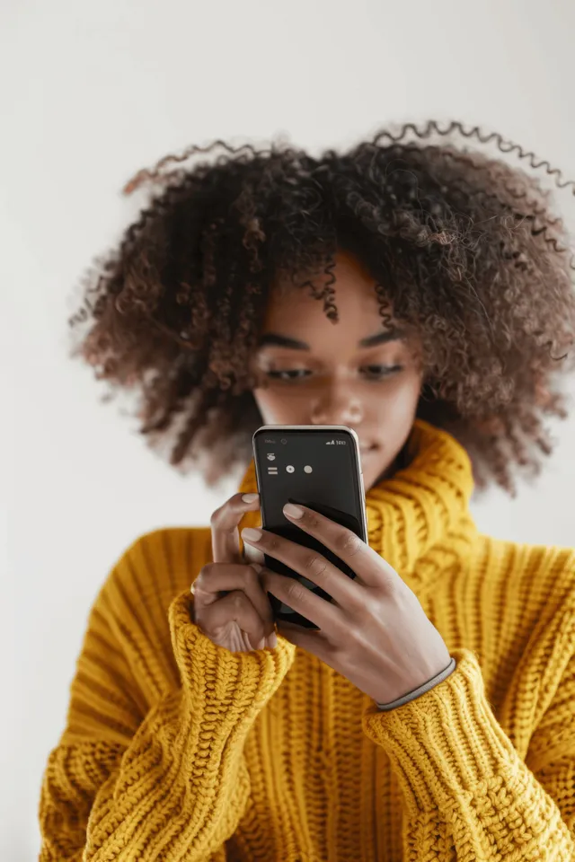Young Woman Checking Smartphone at Home in Yellow Turtleneck