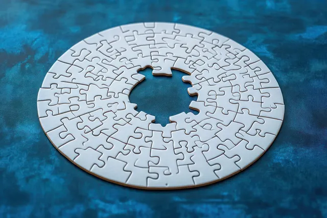 Circular white jigsaw puzzle with a missing piece forming a hollow center on textured blue surface.