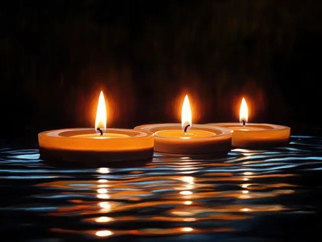 Three lit candles float on dark water, casting warm reflections across gentle ripples.