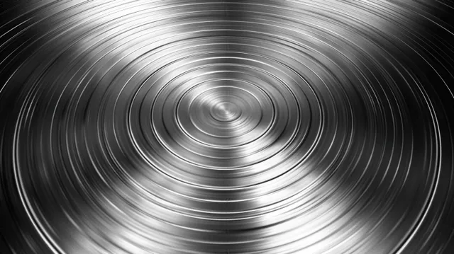 Brushed steel plate with concentric circular grooves creating radial reflections across a shiny surface.