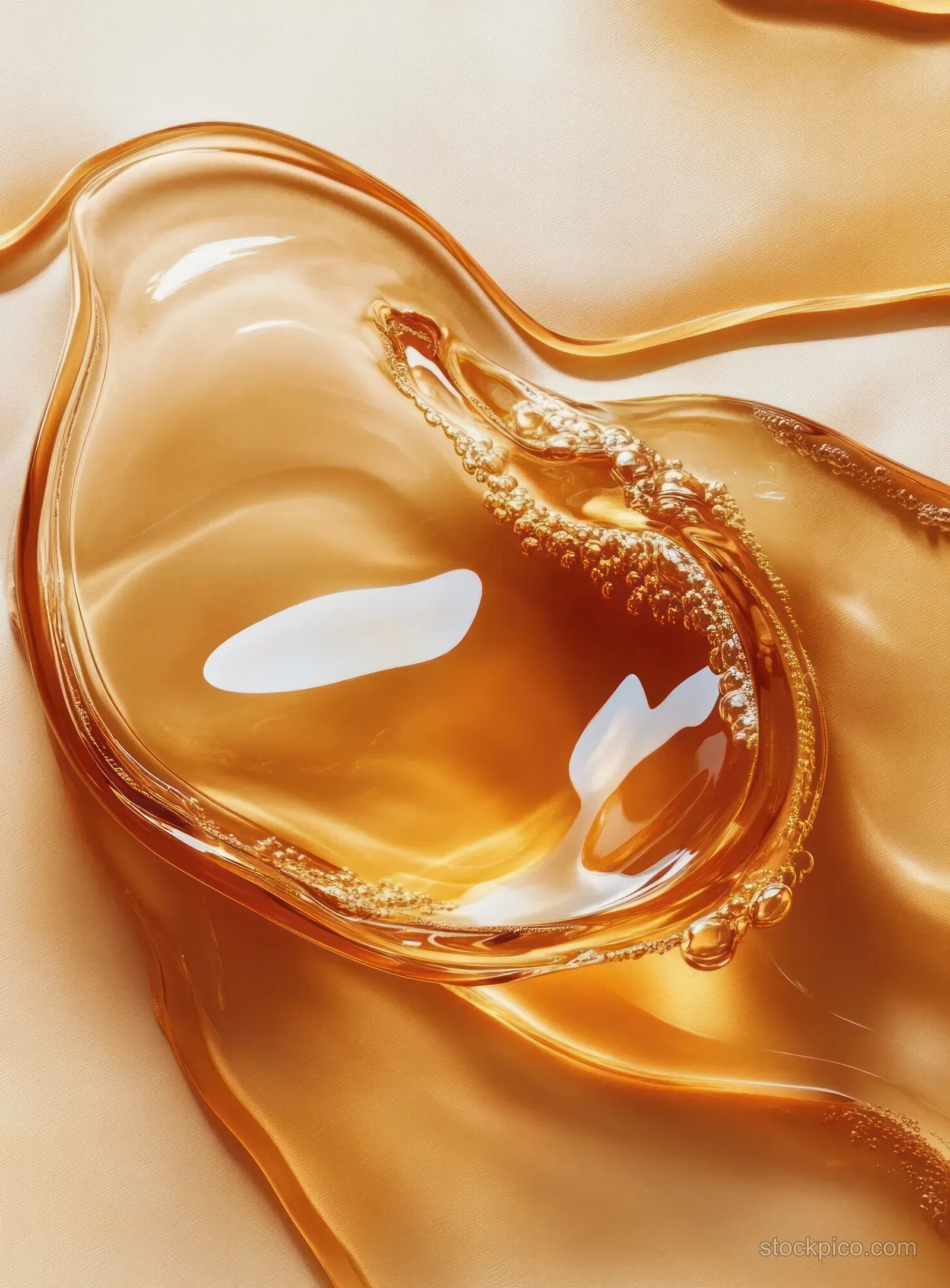 A glossy amber droplet with small bubbles and bright reflections sits on a smooth liquid surface.