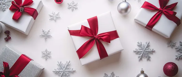Christmas gift boxes with red bows rest on a white surface scattered with silver snowflakes.