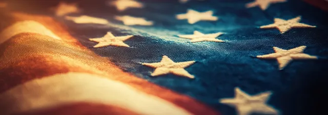 Close-up of a waving American flag with stars visible under warm sunlight and vintage soft-focus texture.