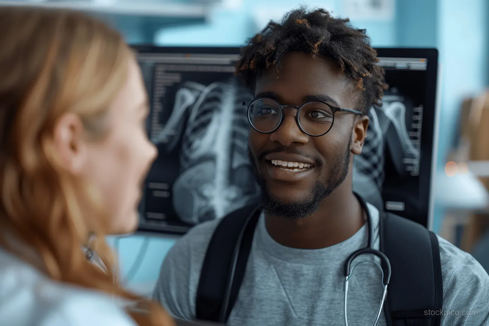 Doctor with stethoscope consults beside a monitor displaying a chest X-ray in a clinic office.