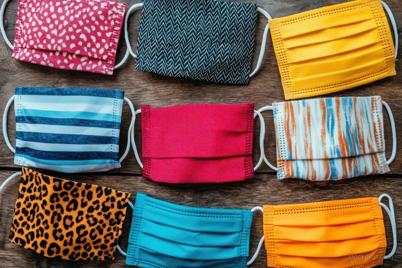 Multiple cloth face masks with striped, plaid, and leopard patterns are laid out on rustic wood.