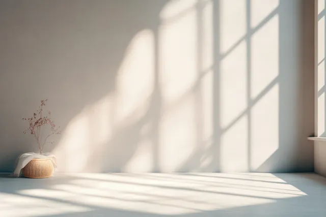 Empty minimalist studio room with peach beige walls, sunlight through a window, and soft shadow bands on the floor.