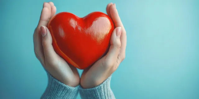 Hands cradling a red heart on blue background for health support awareness