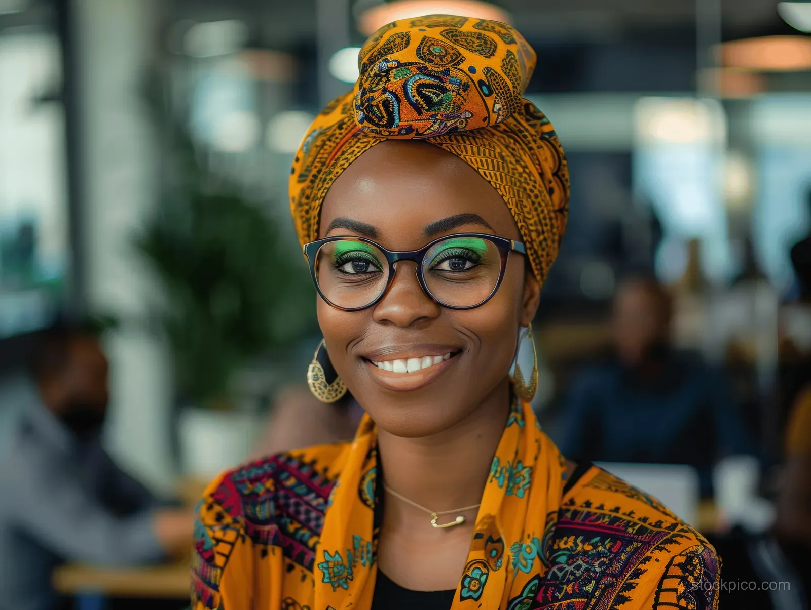 A smiling businesswoman in a patterned turban and glasses leads a team meeting in a modern office.