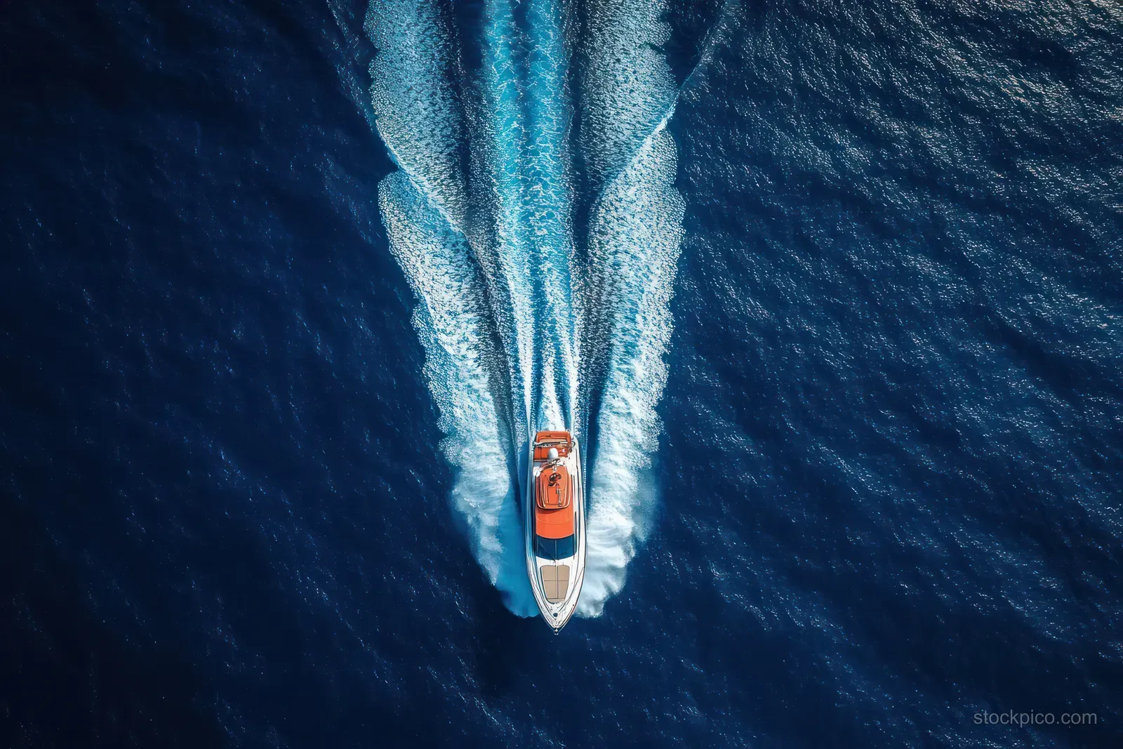 Top-down view of a motorboat speeding through deep blue ocean, trailing white foam and wake.