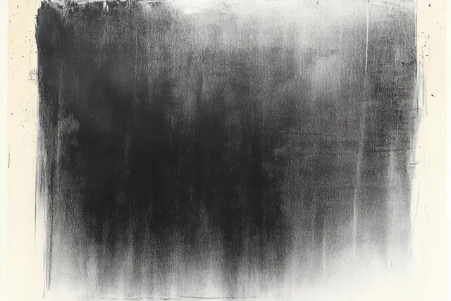 Monochrome ink blot with dense smudges fading softly into white paper backdrop