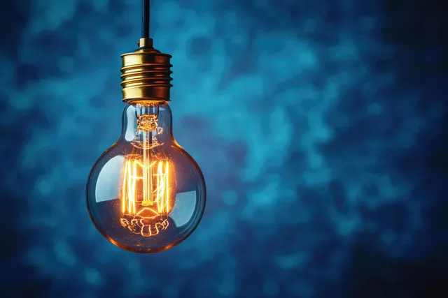 Glowing vintage incandescent bulb hanging in a blue blur background, filament visible inside