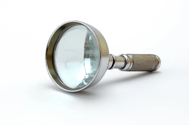 Silver magnifying glass lying on white surface, reflecting light across its circular lens with Tool And Technique
