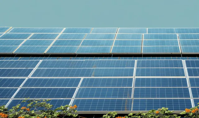 Solar panels cover a commercial building rooftop, reflecting sunlight across blue sky.