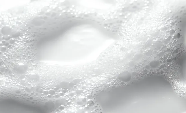 White foam bubbles cluster on a liquid surface, forming soft airy patterns with shimmering reflections.
