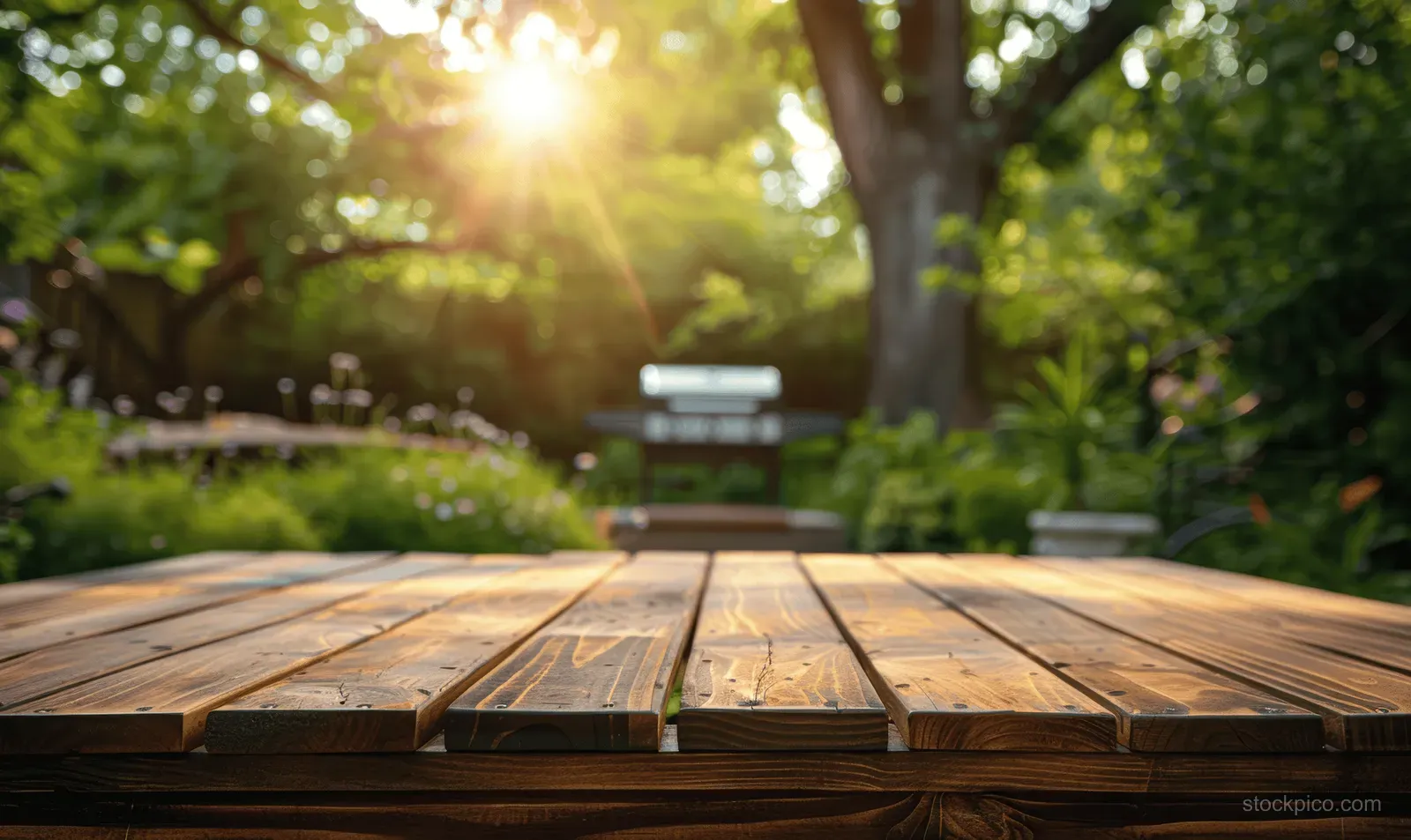 Sunlit wooden outdoor table in a lush garden with a barbecue grill visible in the background.