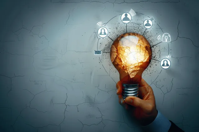 Hand holding a glowing light bulb with a cracked orange globe and surrounding circuit-style education icons.