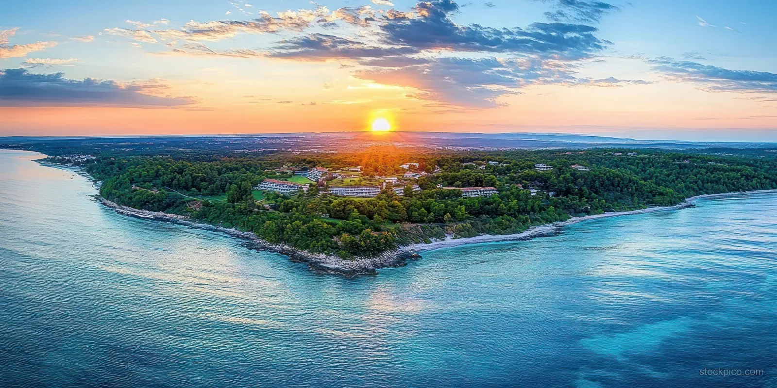 Drone aerial view of the Istria coastline at golden hour, with sun glare over blue water and green shores.