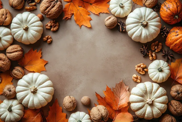 Overhead view of white and orange pumpkins with walnuts, acorns, and autumn leaves arranged around a blank space.