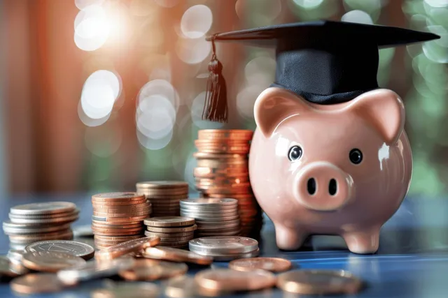 A piggy bank wearing a graduation cap surrounded by stacked coins on a desk.