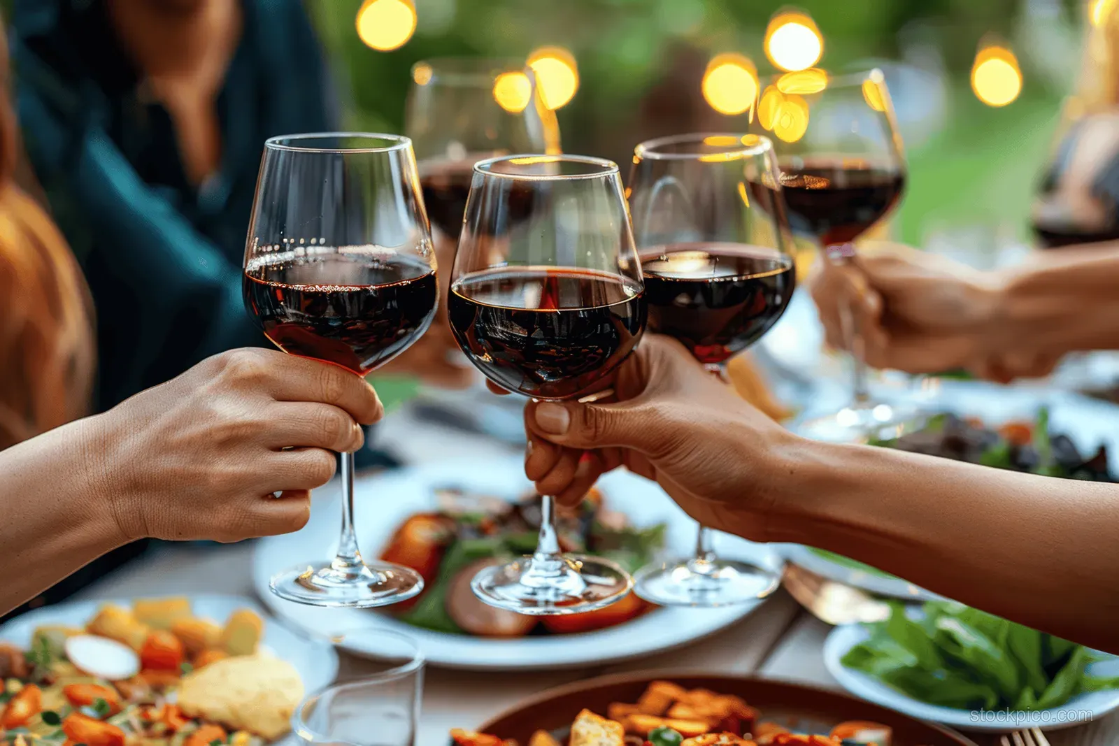 Friends raise and clink red wine glasses over a BBQ dinner table during a summer rooftop gathering.